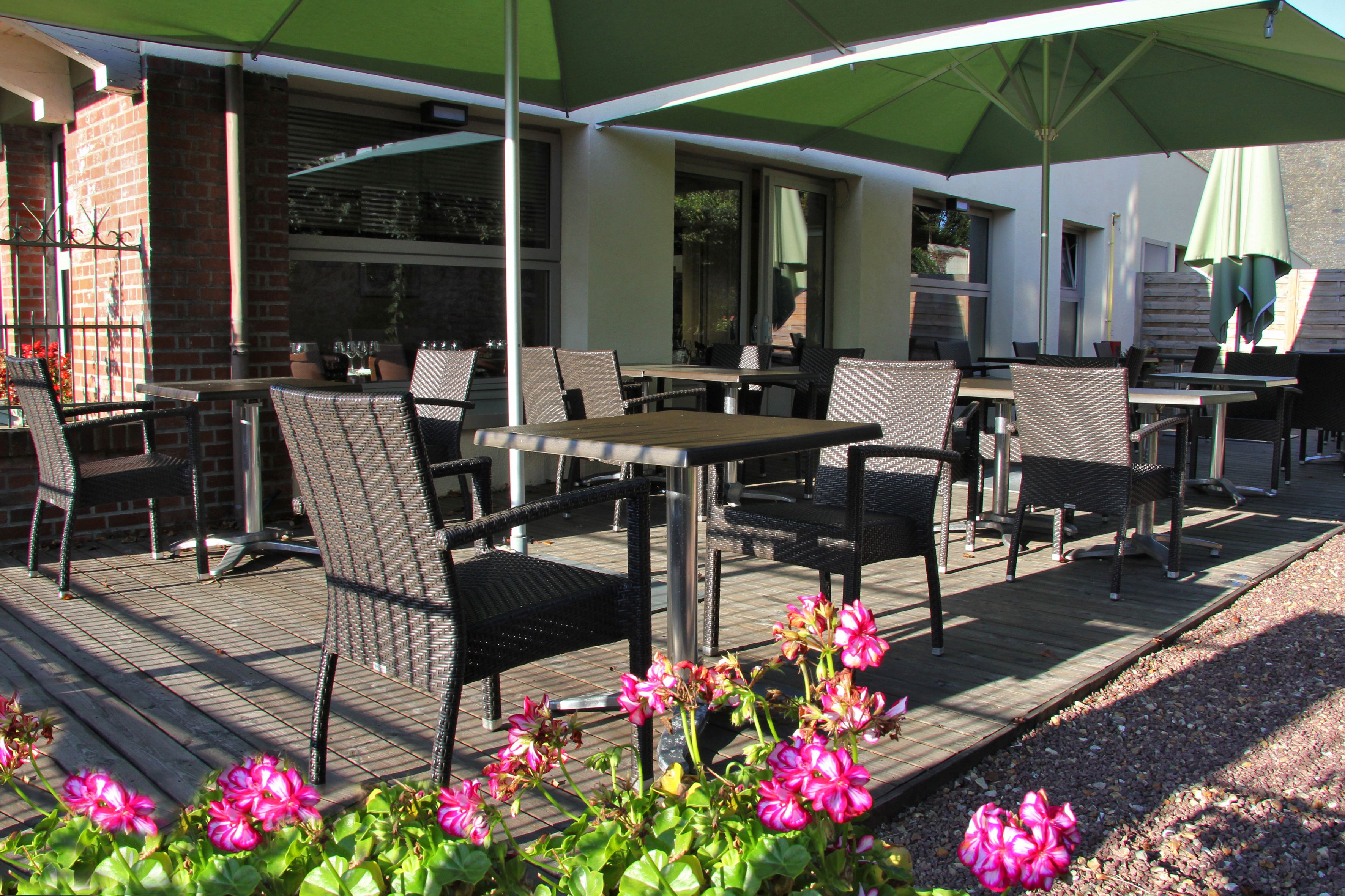 An outdoor patio area with wicker chairs and tables, a green umbrella, and pink flowers.
