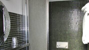 Un baño con lavamanos blanco, un espejo y una zona de ducha con pared de azulejos.