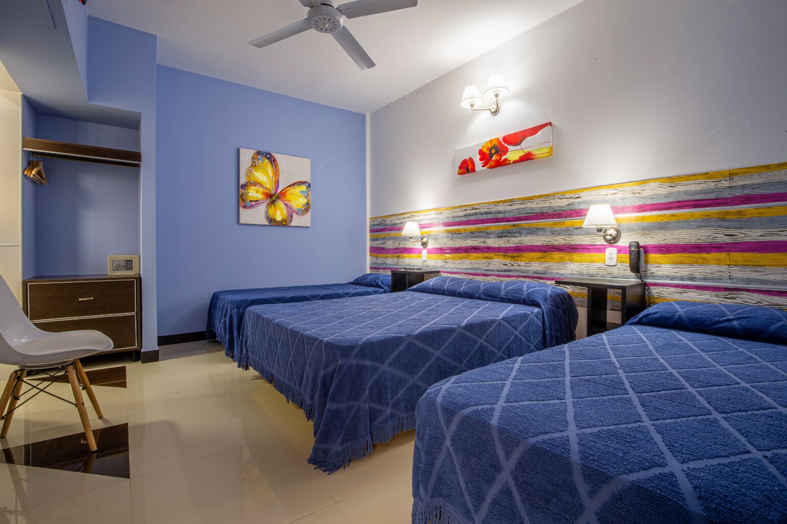 A hotel room with two beds, a desk, a chair, a ceiling fan, and artwork on the walls.