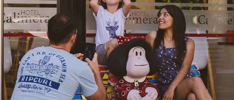 A person taking a photo of a child and a woman sitting on a bench with a mascot.