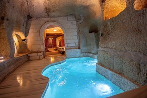 A spa area with a stone wall, a wooden floor, and a pool. - Gamirasu Junior (Ürgüp)