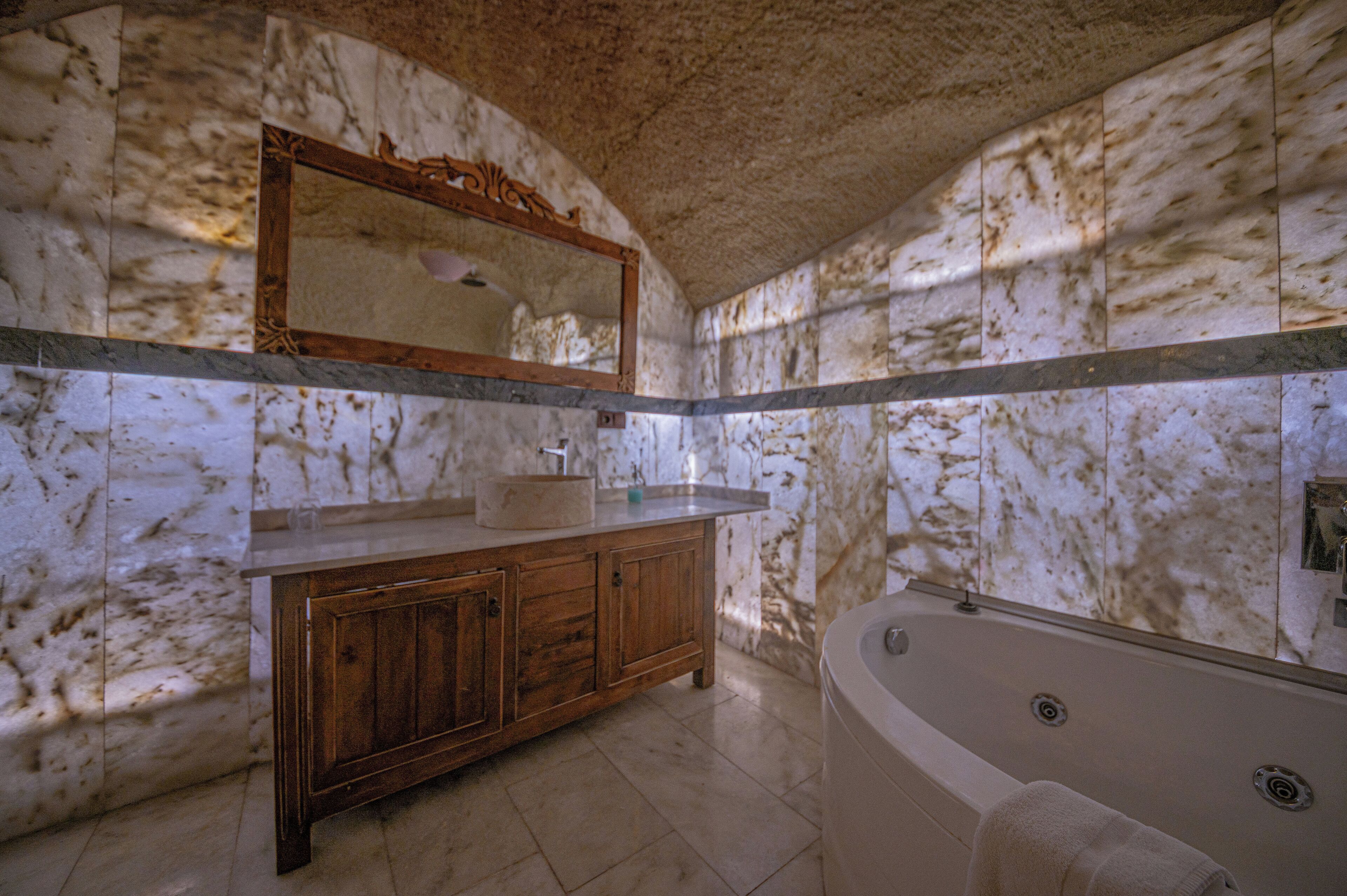 A bathroom with marble walls, a wooden vanity, a large mirror, and a freestanding bathtub.