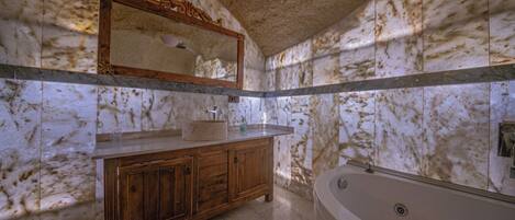 A bathroom with marble walls, a wooden vanity, a large mirror, and a freestanding bathtub.