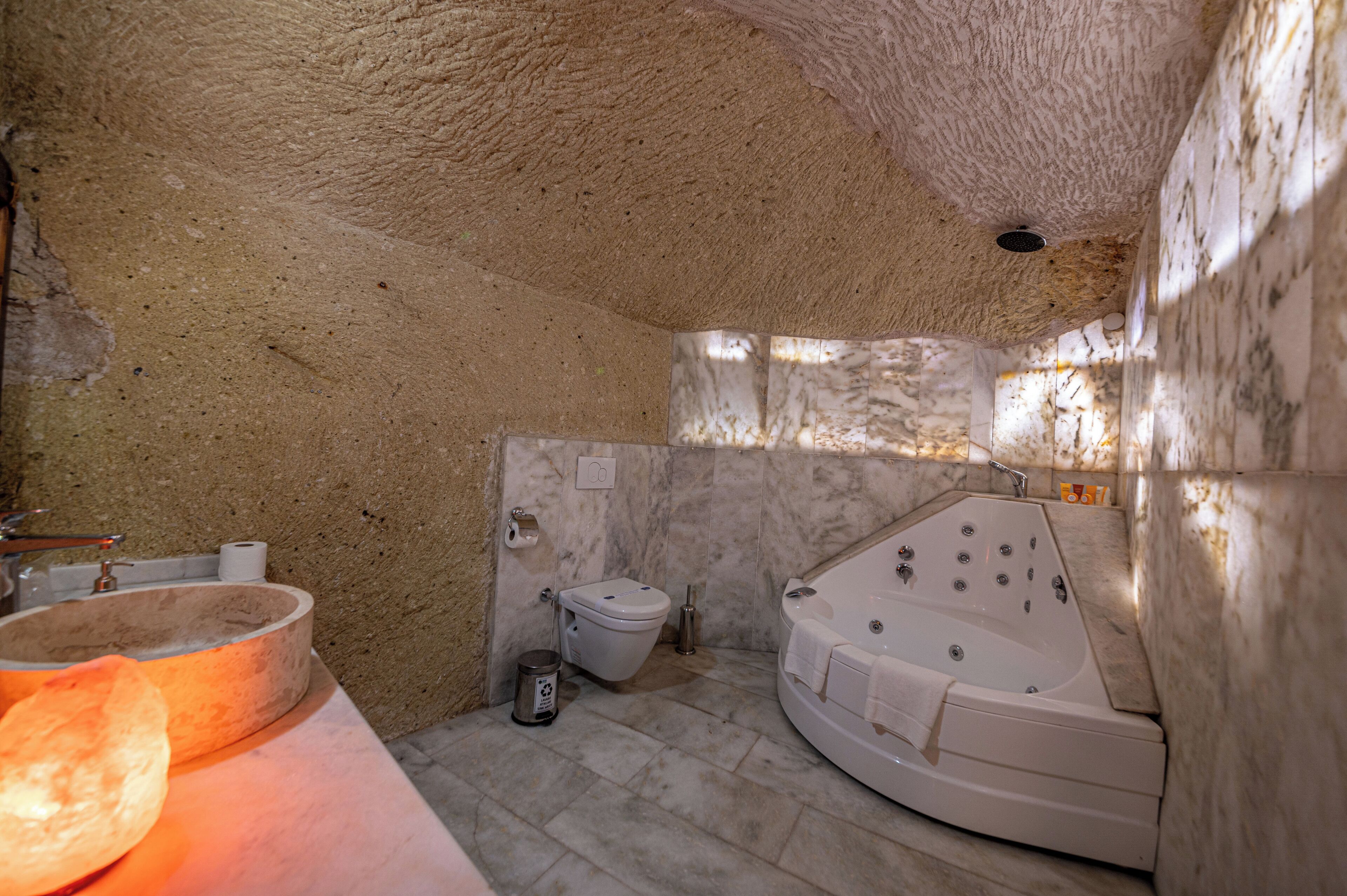 A bathroom with a stone sink, toilet, and a large bathtub.