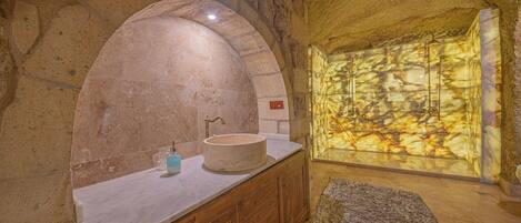 Un baño con lavamanos de piedra, armarios de madera y pared de piedra.