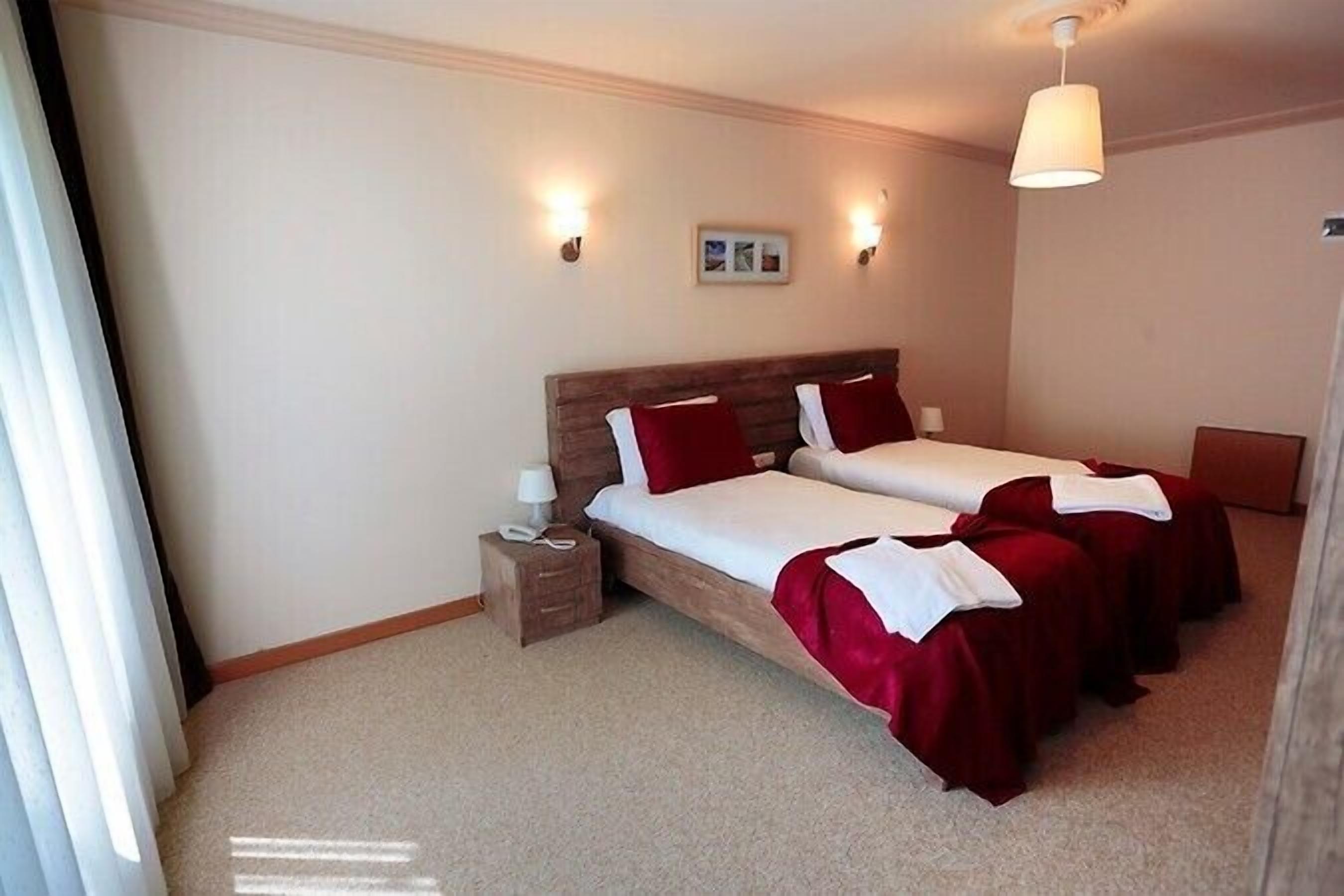 Habitación de hotel con dos camas individuales, una mesita de noche con lámpara e iluminación en el techo.
