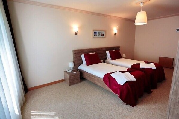 Une chambre d’hôtel avec deux lits simples, une table de chevet avec une lampe et un luminaire au plafond.