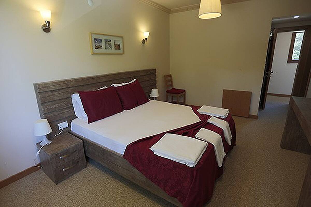 A double bed with a wooden headboard, two bedside tables with lamps, a red bedspread, and a framed picture on the wall.