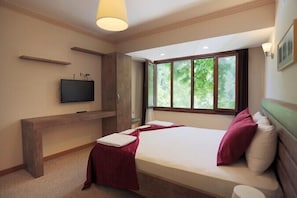 Un dormitorio con cama, televisión, ventana y banco de madera.