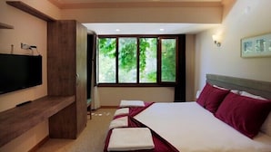 Ein Hotelzimmer mit einem großen Bett, einem Fernseher auf einem Holzboden und einem Fenster mit Blick auf Grünflächen.