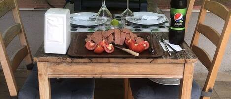 Mesa de comedor de madera al aire libre, con sillas, una parrilla y una botella de Pepsi.