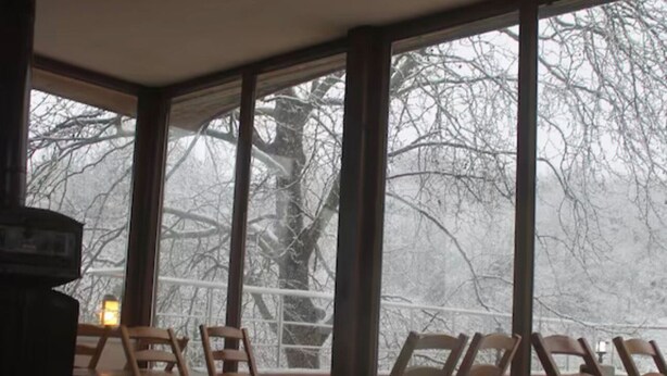 Ein Zimmer mit großen Fenstern, Holzstühlen und einem Tisch.