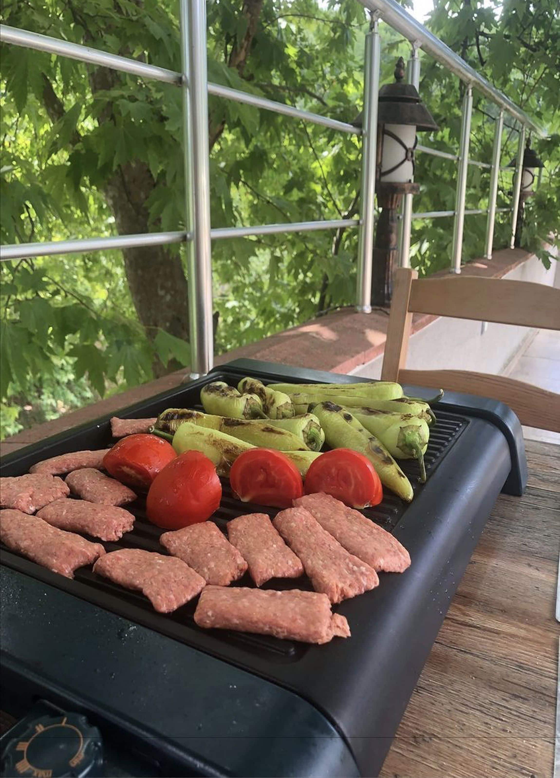 A grill with sausages, tomatoes, and asparagus on a wooden table outdoors.