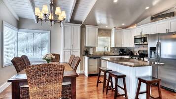 A modern kitchen with white cabinets, a stainless steel refrigerator, and a dining area with wicker chairs and a wooden table.