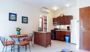 A modern kitchen with wooden cabinets, a built-in microwave, and a coffee maker. There is a dining area with a table and chairs, and a water dispenser on the counter.