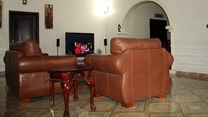 A living room with two brown leather sofas, a wooden coffee table, a flat-screen TV, and a fireplace. - The Whitestone Inn (Adentan)