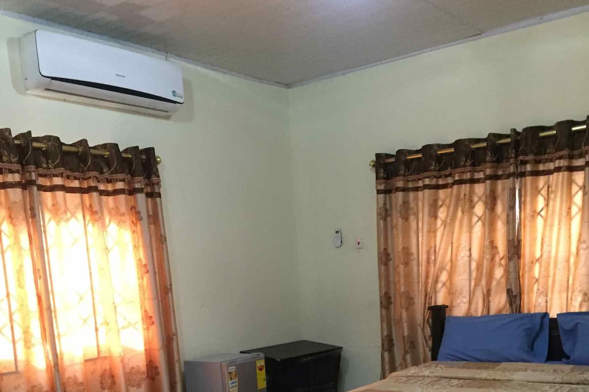 A room with a bed, curtains, an air conditioner, and a small refrigerator.