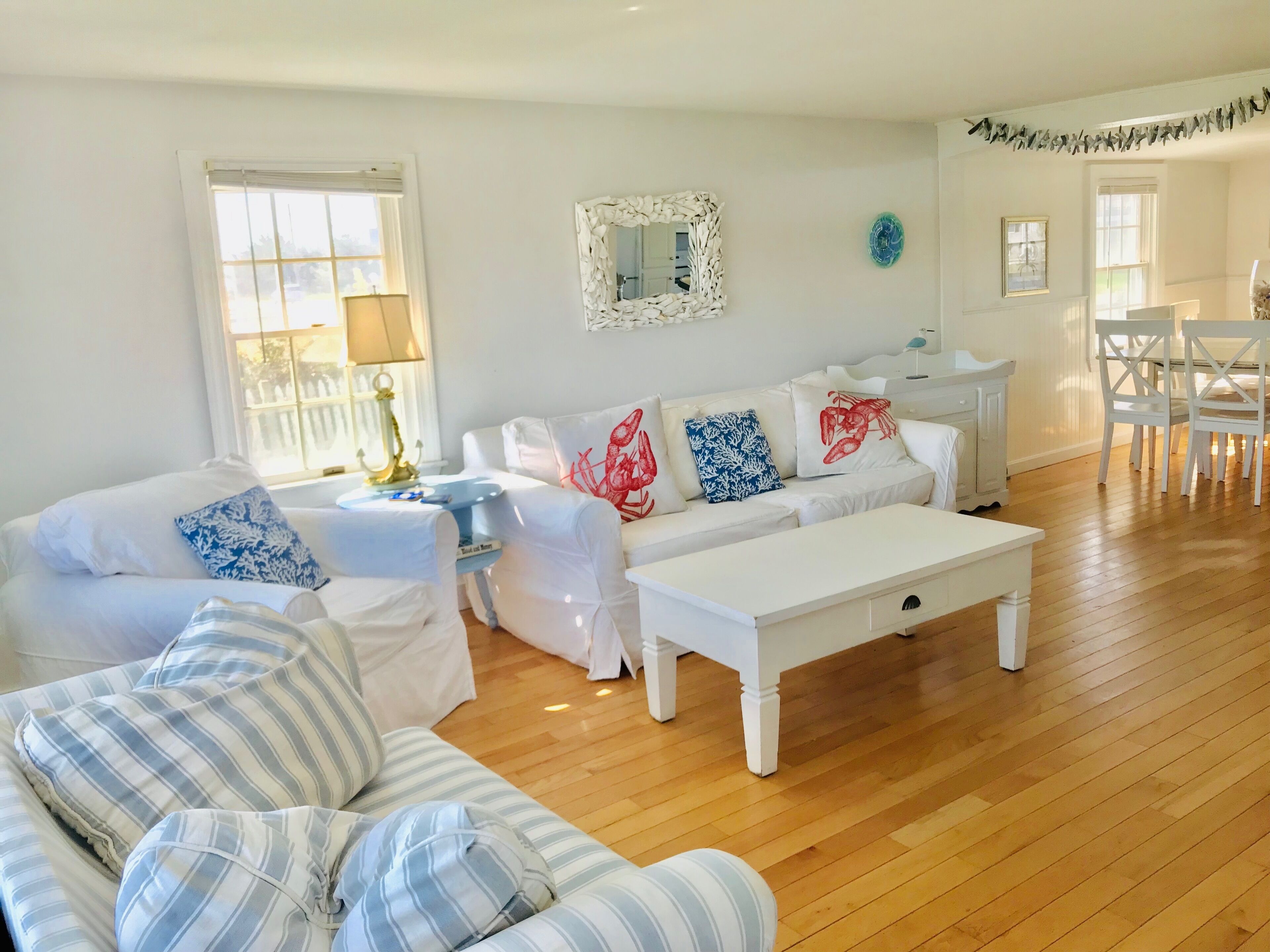 A living room with a white sofa, striped armchair, and a coffee table. There is a dining area with white chairs and a table.