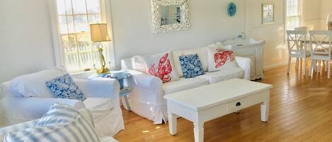 A living room with a white sofa, striped armchair, and a coffee table. There is a dining area with white chairs and a table.