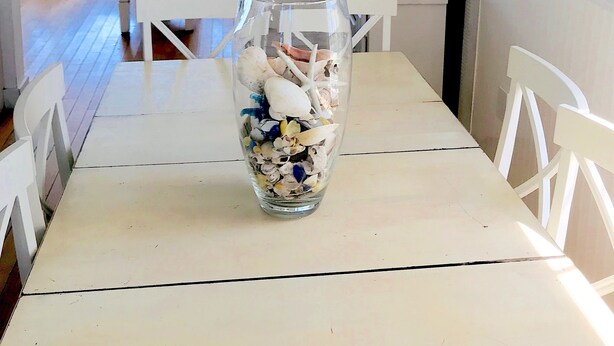 Una sala de estar con un sofá blanco, una mesa de centro con un florero de vidrio y vista al exterior a través de un ventanal grande.