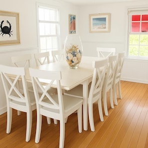 A dining area with a white table and chairs, a vase with flowers, and framed artwork on the walls.