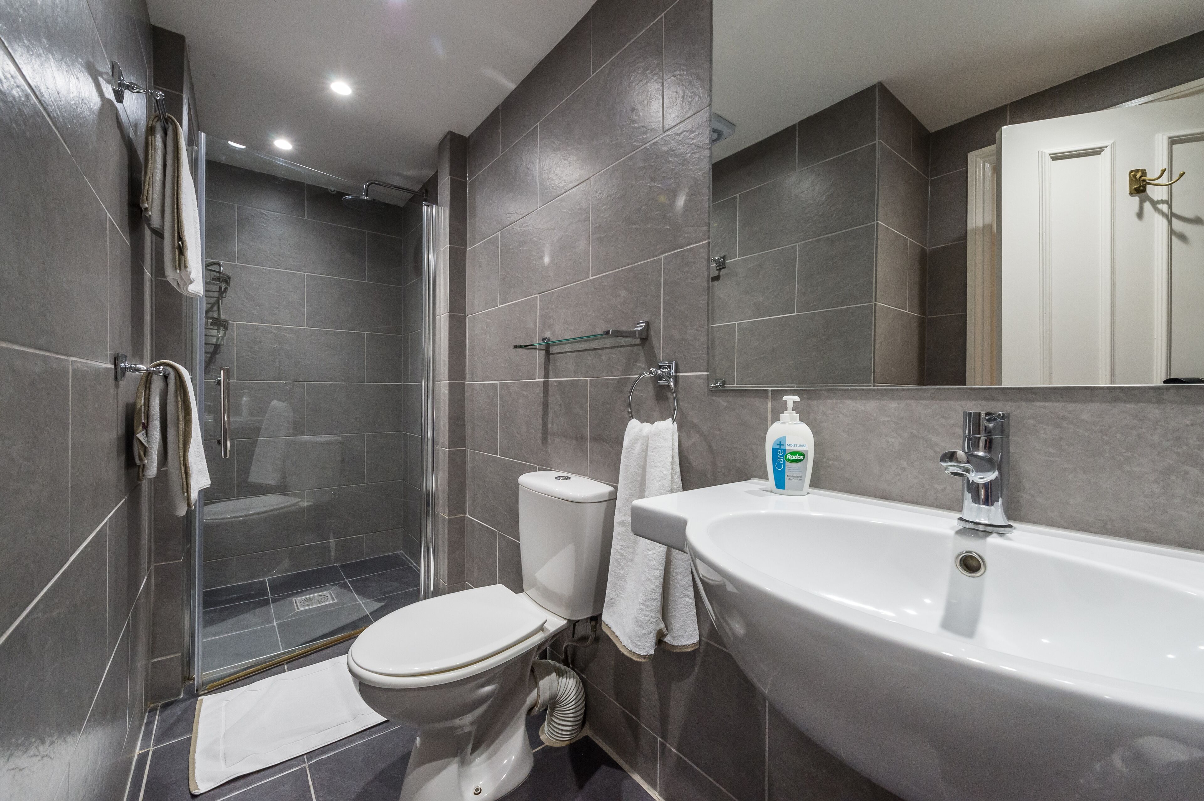 Une salle de bain moderne avec une douche à parois de verre, des toilettes et un lavabo blanc avec un miroir au-dessus.