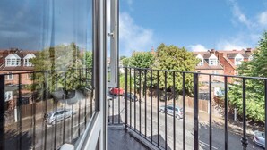 Un balcón con barandilla metálica que da a una calle con coches aparcados y edificios residenciales.