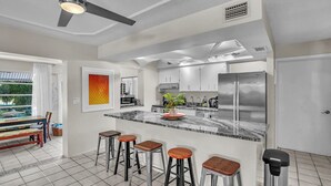 Uma cozinha moderna com uma ilha central, banquetas de bar, eletrodomésticos de aço inoxidável e um ventilador de teto.