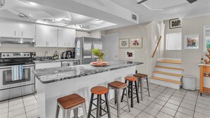 Cozinha moderna com eletrodomésticos de aço inoxidável, bancada de mármore e ilha central com banquetas.