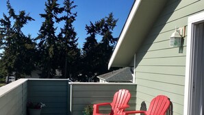 A covered patio with two red Adirondack chairs, a potted plant, and a trash can. - Carlsborg Montian  View Apartment   (Sequim)