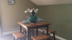 A dining area with a wooden table, four benches, a teal vase with flowers, and a wall sign. - Carlsborg Montian  View Apartment   (Sequim)