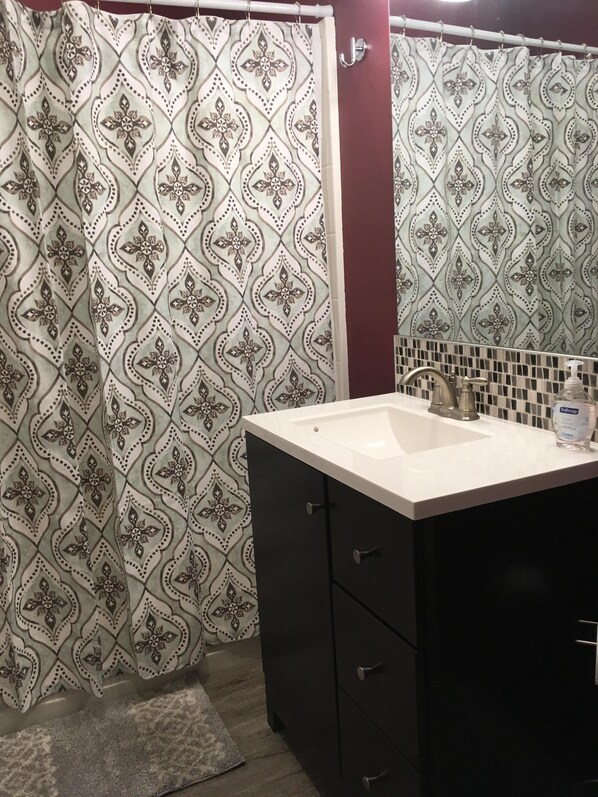 A bathroom with a patterned shower curtain, a white sink with a soap dispenser, and dark cabinets. - Carlsborg Montian View Apartment (Sequim)