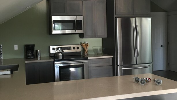 A modern kitchen with a central island, stainless steel appliances, and wooden stools. - Carlsborg Montian  View Apartment   (Sequim)