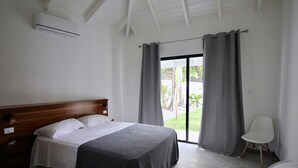 A bedroom with a wooden headboard bed, a white chair, and a view of the outdoors through a sliding glass door. - Casa Panama Modern 5 bedroom villa 250m beach-  (Las Terrenas)