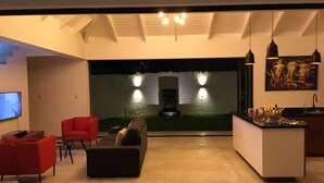 A modern living room with a sofa, red chairs, a flat-screen TV, and a kitchen area with a sink and counter. - Casa Panama Modern 5 bedroom villa 250m beach-  (Las Terrenas)