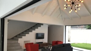A modern living room with a staircase, a flat-screen TV, and a large window overlooking a garden. - Casa Panama Modern 5 bedroom villa 250m beach-  (Las Terrenas)