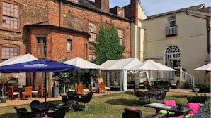 An outdoor seating area with tables and chairs, some under umbrellas, and a brick building in the background. - Kings Newmarket (Newmarket)