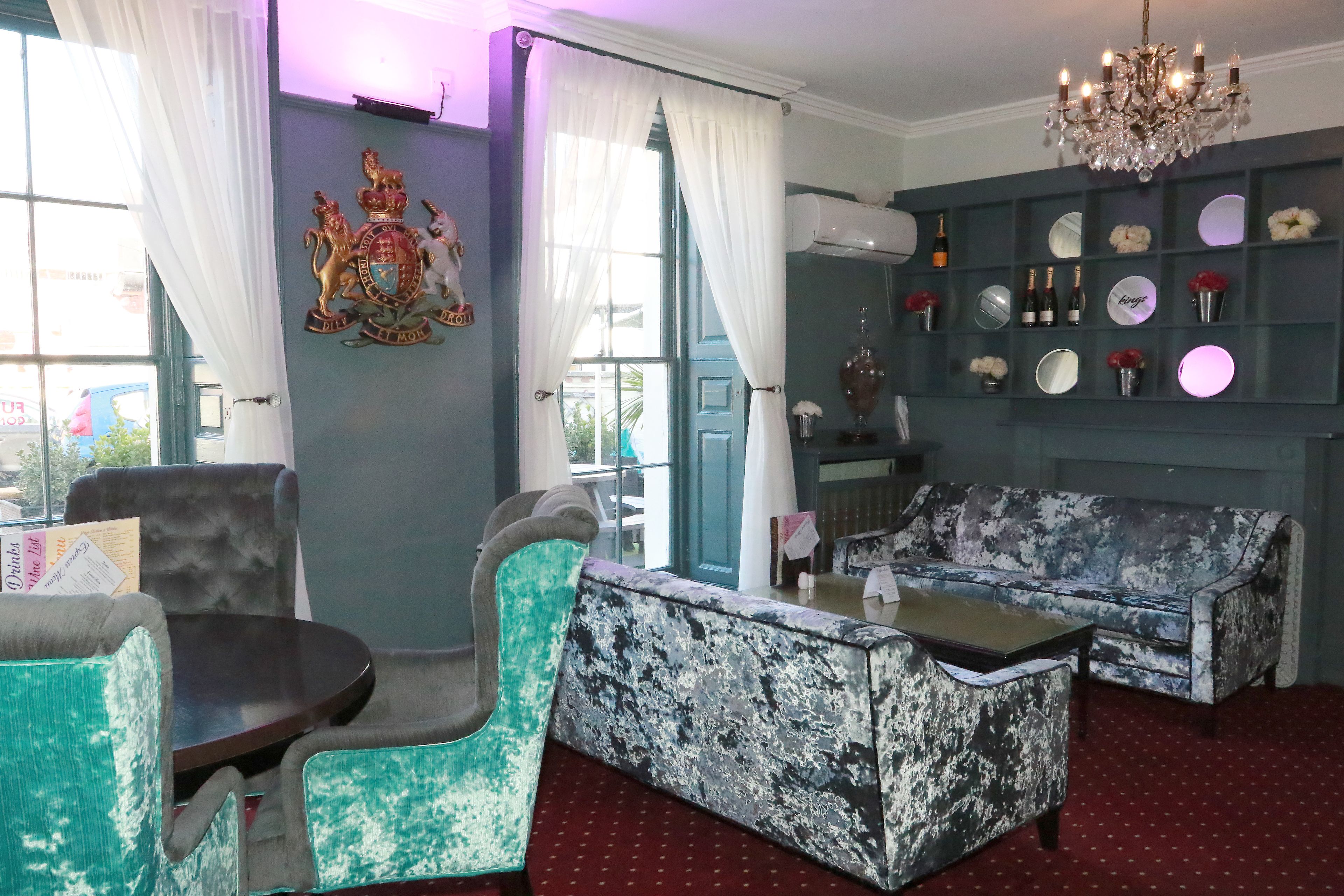 Quarto com sofá de padrão azul e branco, poltrona verde-água e uma pequena mesa redonda. Há um candelabro sobre o sofá e um emblema decorativo na parede.