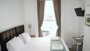 A hotel room with a bed, a desk, a chair, a TV, and a window with curtains. - Kings Newmarket (Newmarket)