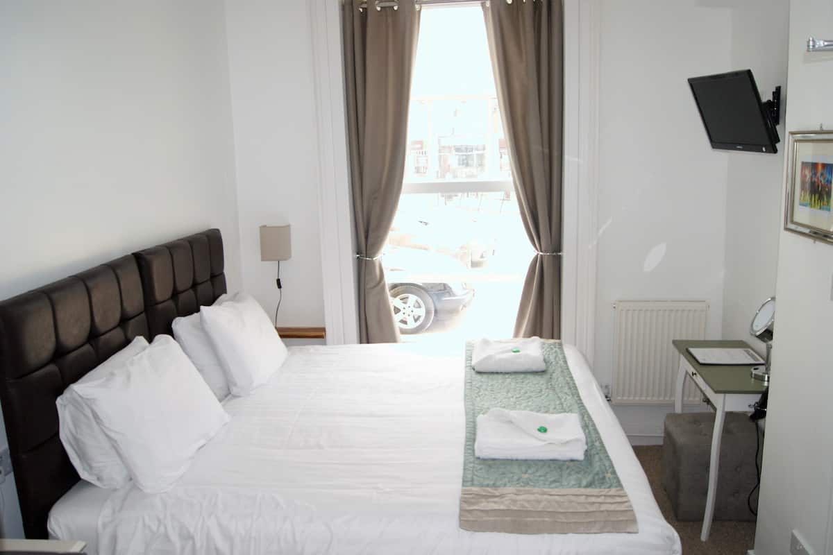 Una camera d'albergo con un letto, una scrivania, una sedia, una televisione e una finestra con tende.