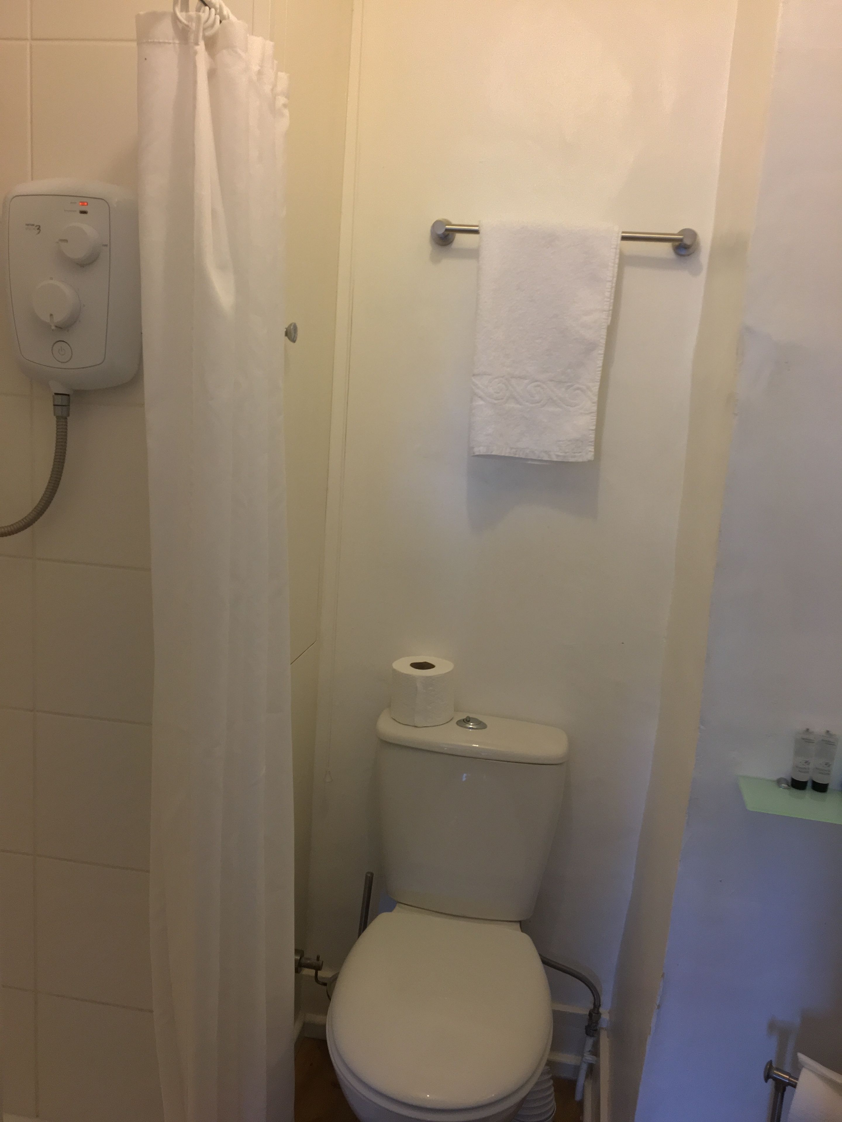 Een badkamer met toilet, douchegordijn, handdoekhouder en toiletrolhouder.