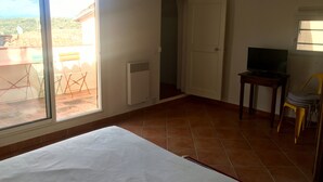 A room with a bed, a television on a small table, a sliding glass door leading to an outdoor area, and a white door. - Authentic village house in the center of Ramatuelle (Ramatuelle)