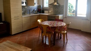A kitchen with wooden cabinets, a stove, a sink, and a dining table with chairs. - Authentic village house in the center of Ramatuelle (Ramatuelle)