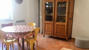 A dining area with a round table covered in a polka dot tablecloth, surrounded by yellow chairs. A wooden cabinet with glass doors is in the background, and a small round ottoman is on the floor. - Authentic village house in the center of Ramatuelle (Ramatuelle)