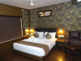 Habitación de hotel con una cama grande, dos mesitas de noche con lámparas, una silla y un ventilador de techo.