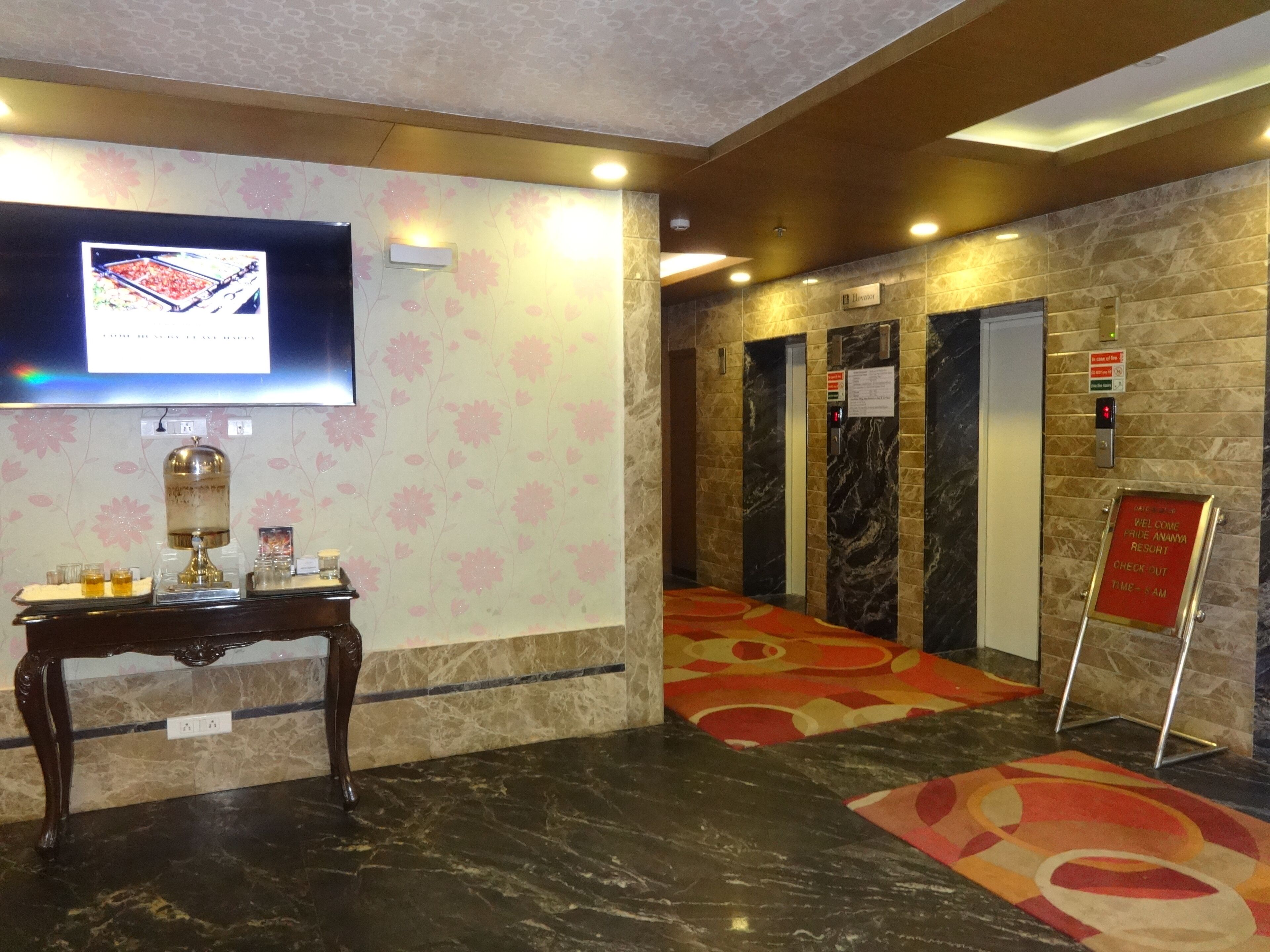 Una hall d'albergo con pavimento in marmo, una reception, un televisore, ascensori e la segnaletica per il check-out.