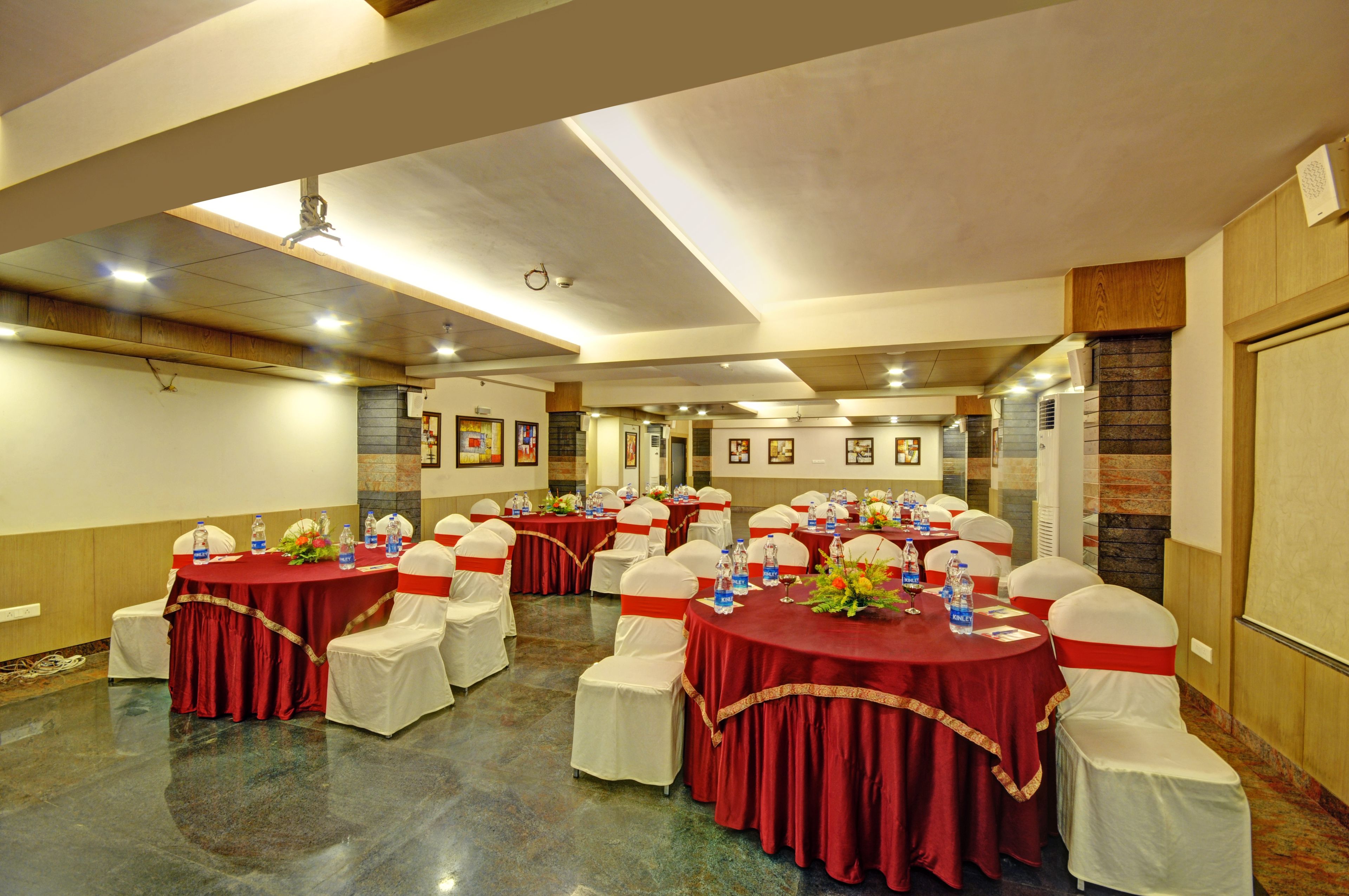 A conference room with multiple round tables, white chairs with red sashes, and water bottles on the tables.