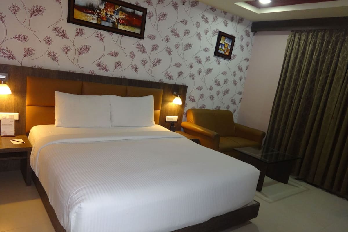 A hotel room with a large bed, two bedside lamps, a chair, a framed picture on the wall, and a curtain.