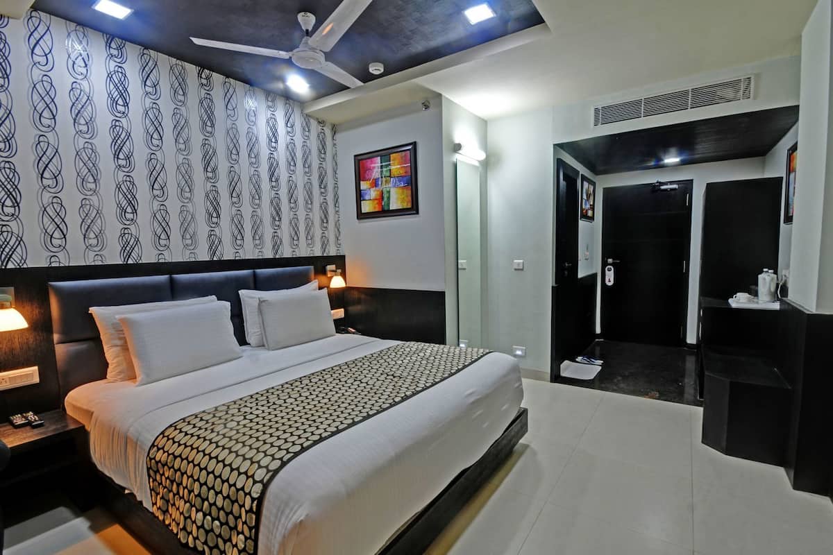 A modern hotel room with a large bed, a ceiling fan, a patterned wall, a bathroom with a mirror and sink, and a black door.