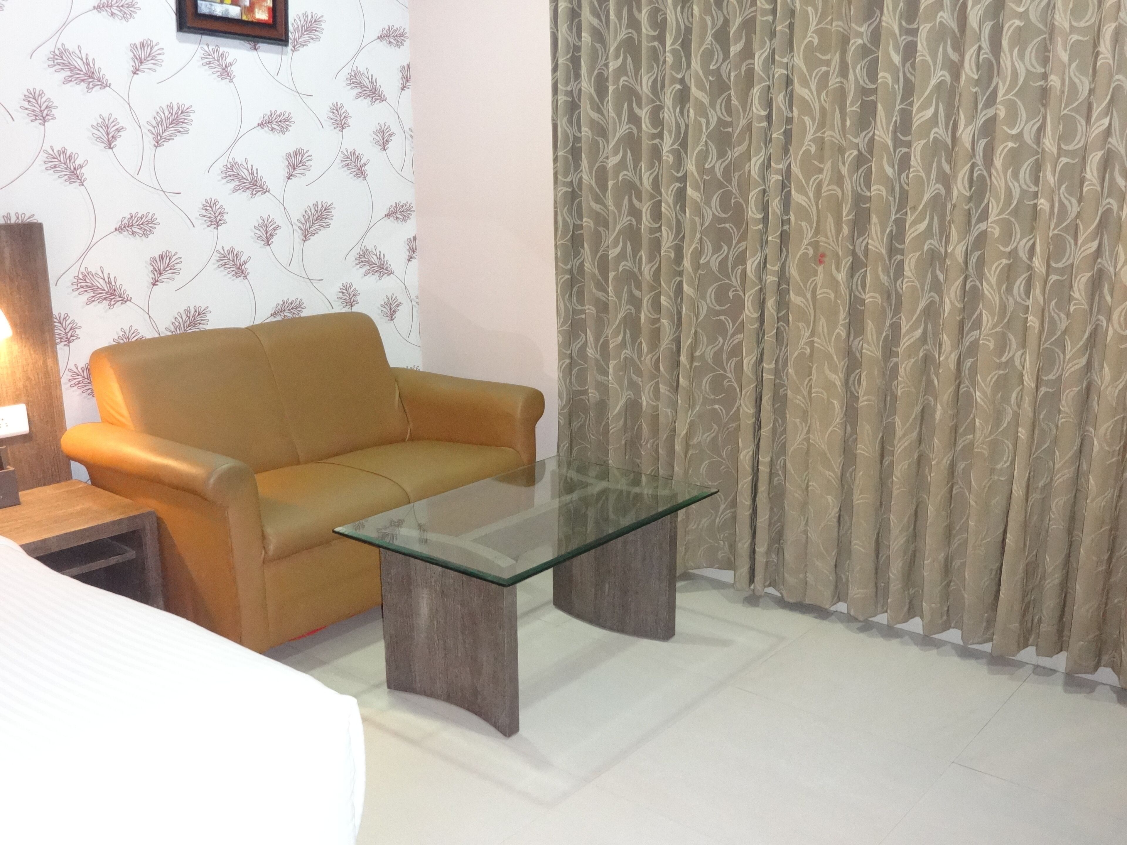 A living room with a sofa, a glass coffee table, a lamp, and curtains.